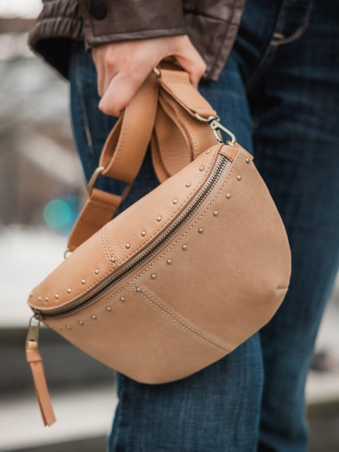 Hand holding tan leather crossbody bag